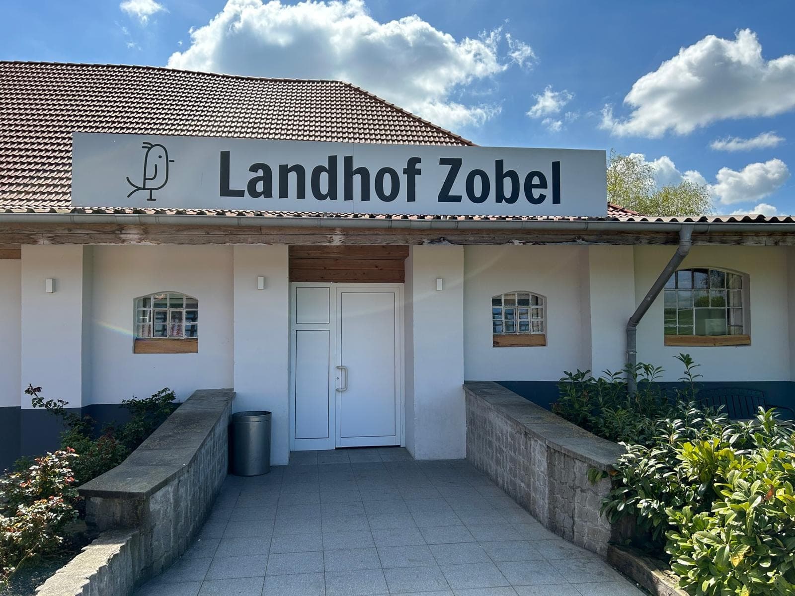 Eingang zum Landhof Zobel mit einem weißen Schild und dem Namen des Hofes und einem Vogel-Logo.