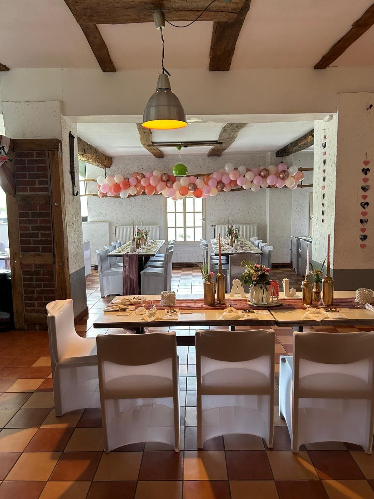 Festlich gedeckter Tisch mit Stühlen und Ballonbogen in Rosa- und Goldtönen.