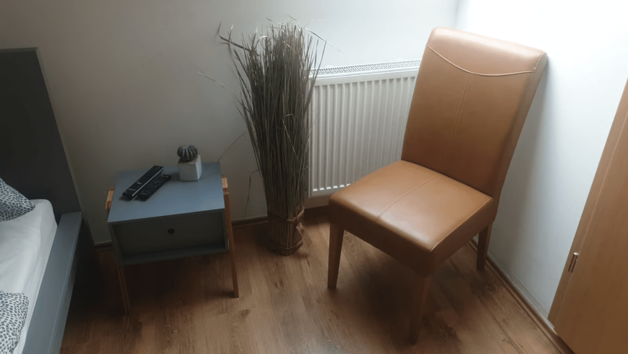 Zimmerecke mit Nachttisch, braunem Lederstuhl und Zimmerpflanze.