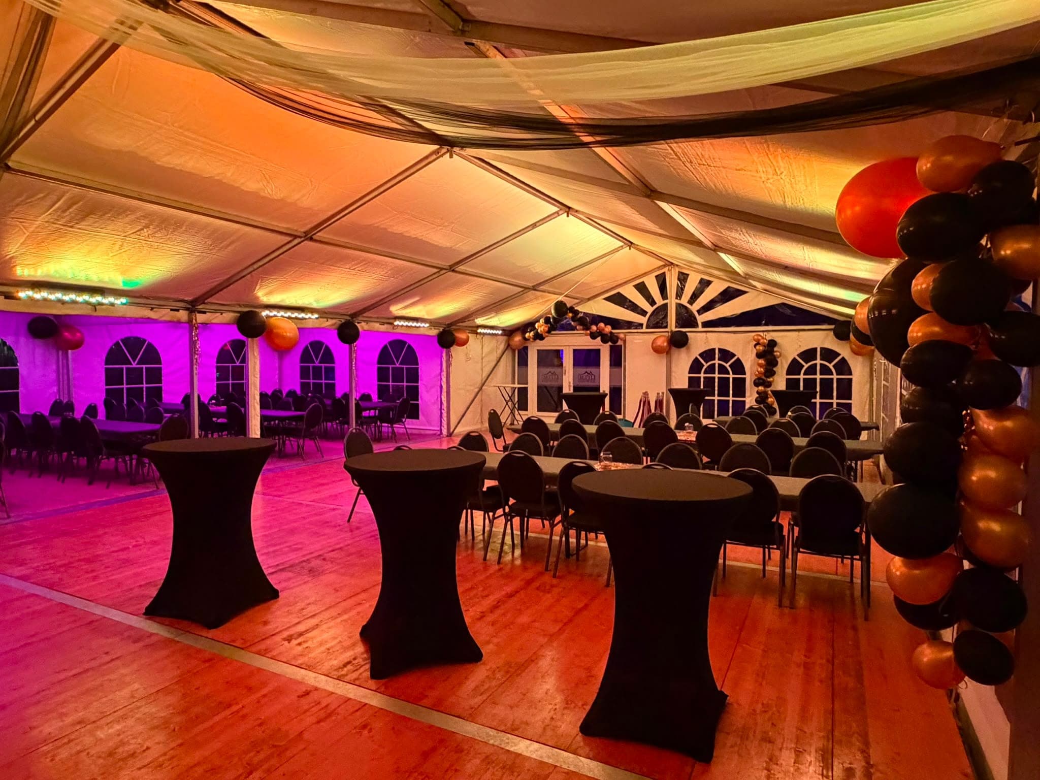 Festzelt mit bunter Beleuchtung, schwarzen Stehtischen und Ballondekoration.
