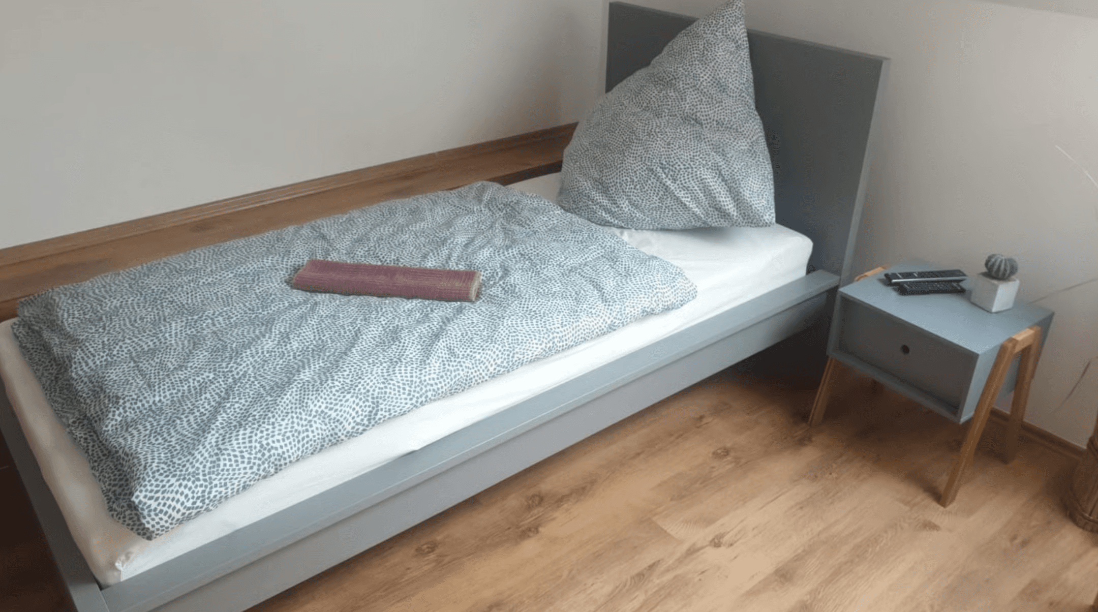 Einzelzimmer mit Bett, Nachttisch und Laminatboden.