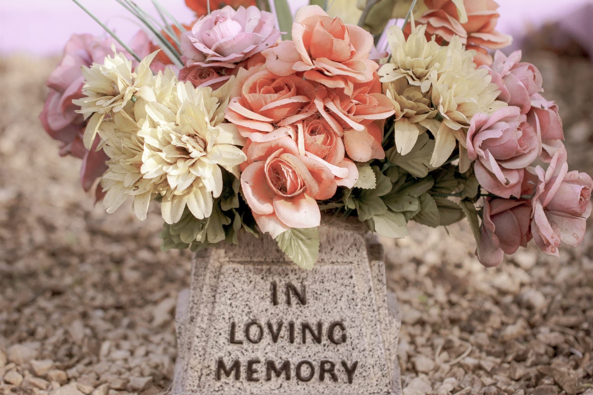 Rosafarbene Kunstblumen auf einem Gedenkstein mit der Aufschrift „In loving memory“.