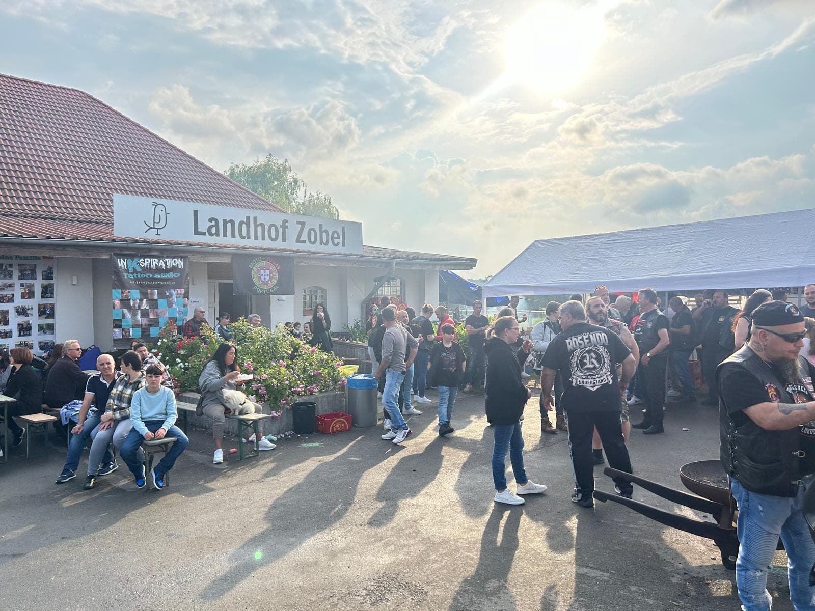 Menschen versammeln sich draußen vor dem Gebäude "Landhof Zobel" unter sonnigem Himmel.