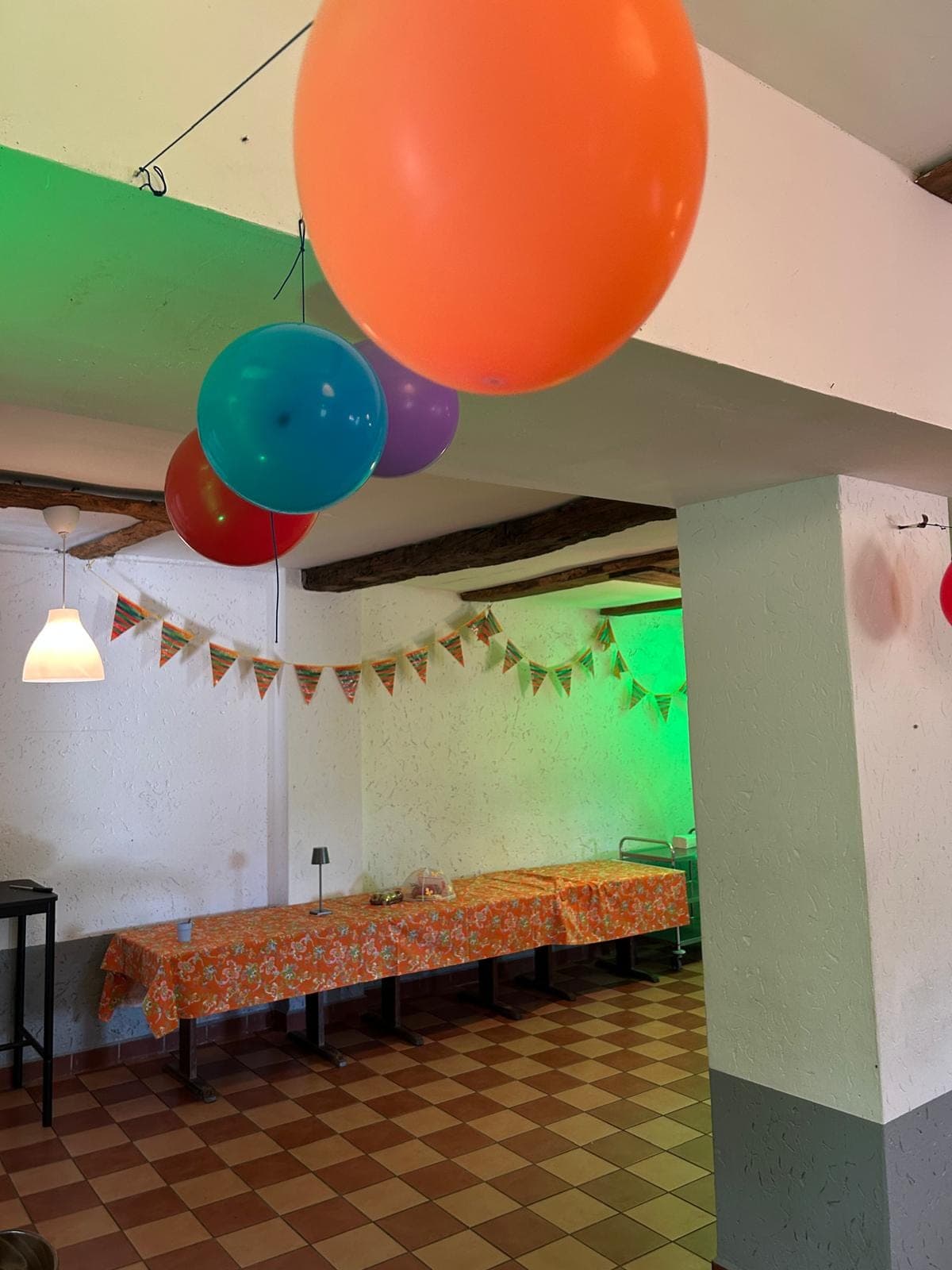 Ein Raum, dekoriert für eine Feier mit bunten Ballons, Girlanden und einem langen Tisch mit orangefarbenem Tischtuch.