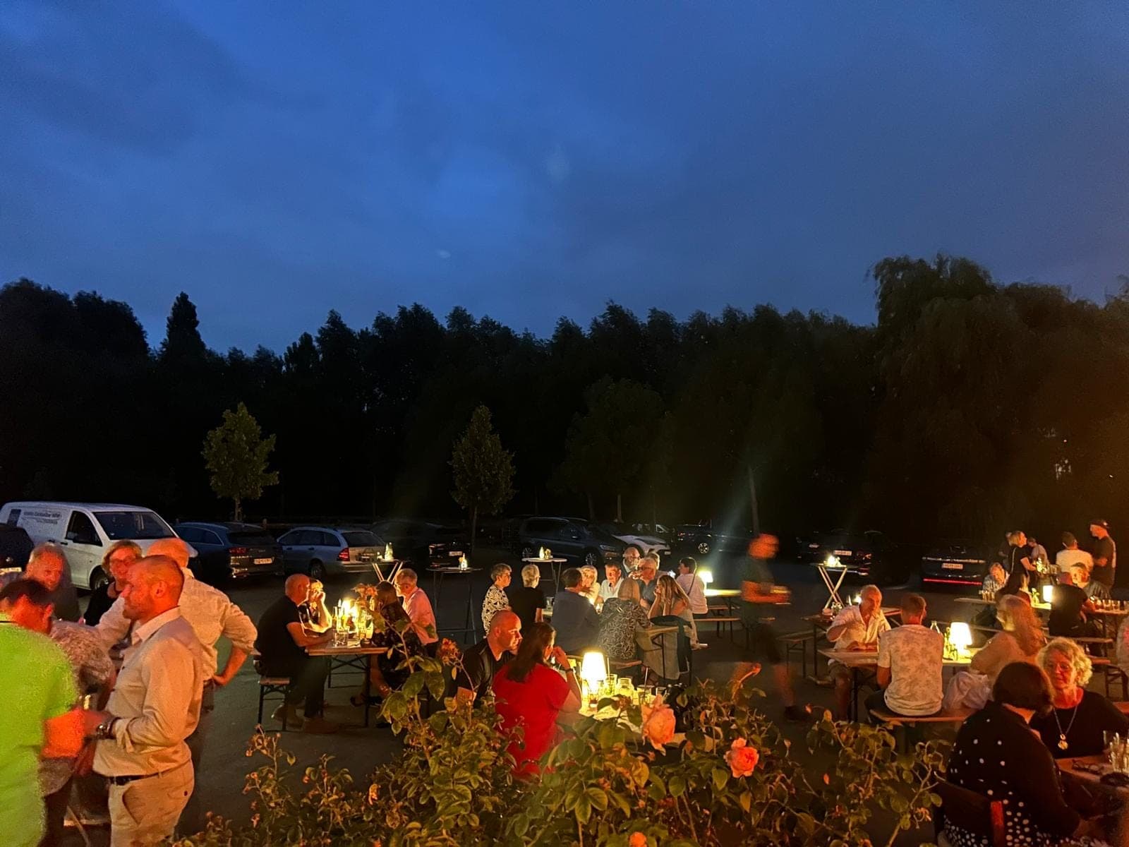 Gäste sitzen am Abend an beleuchteten Biertischen im Freien auf dem Hofgelände.